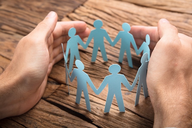 Businessman’s hands protecting a paper-cut team arranged in a circle